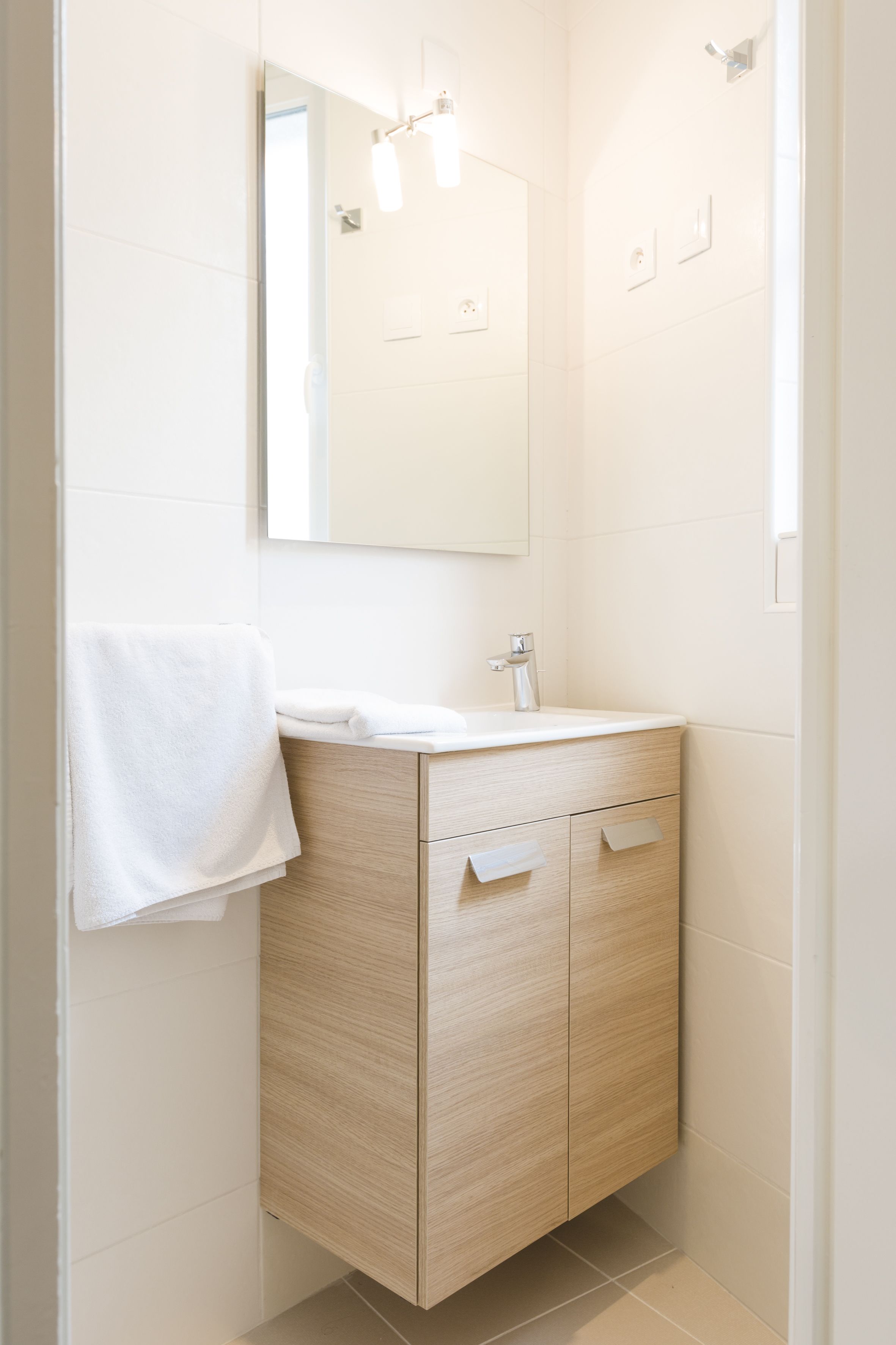 A modern bathroom with a wooden vanity, a white sink, and a mirror above it.