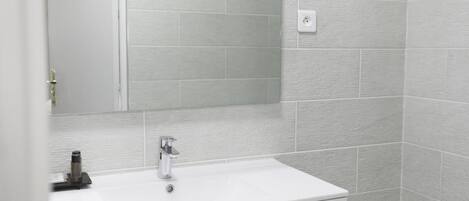 Une salle de bain avec un lavabo blanc, un miroir et des murs recouverts de carreaux gris.
