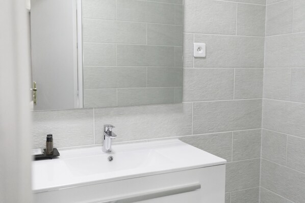 Baño con lavamanos blanco, espejo y paredes con azulejos grises.