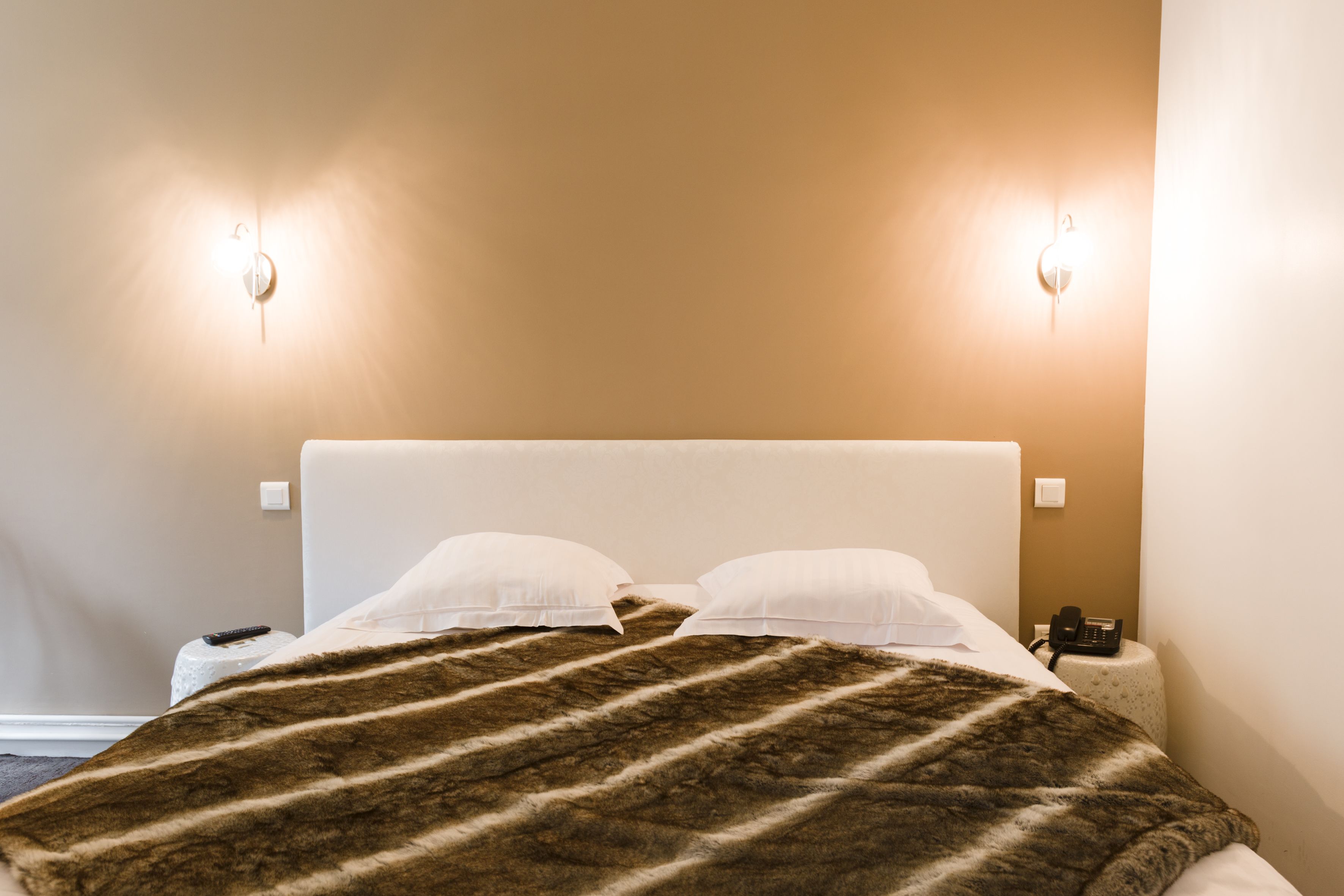 A hotel room with a bed, two bedside lamps, a telephone, and a remote control on a nightstand.