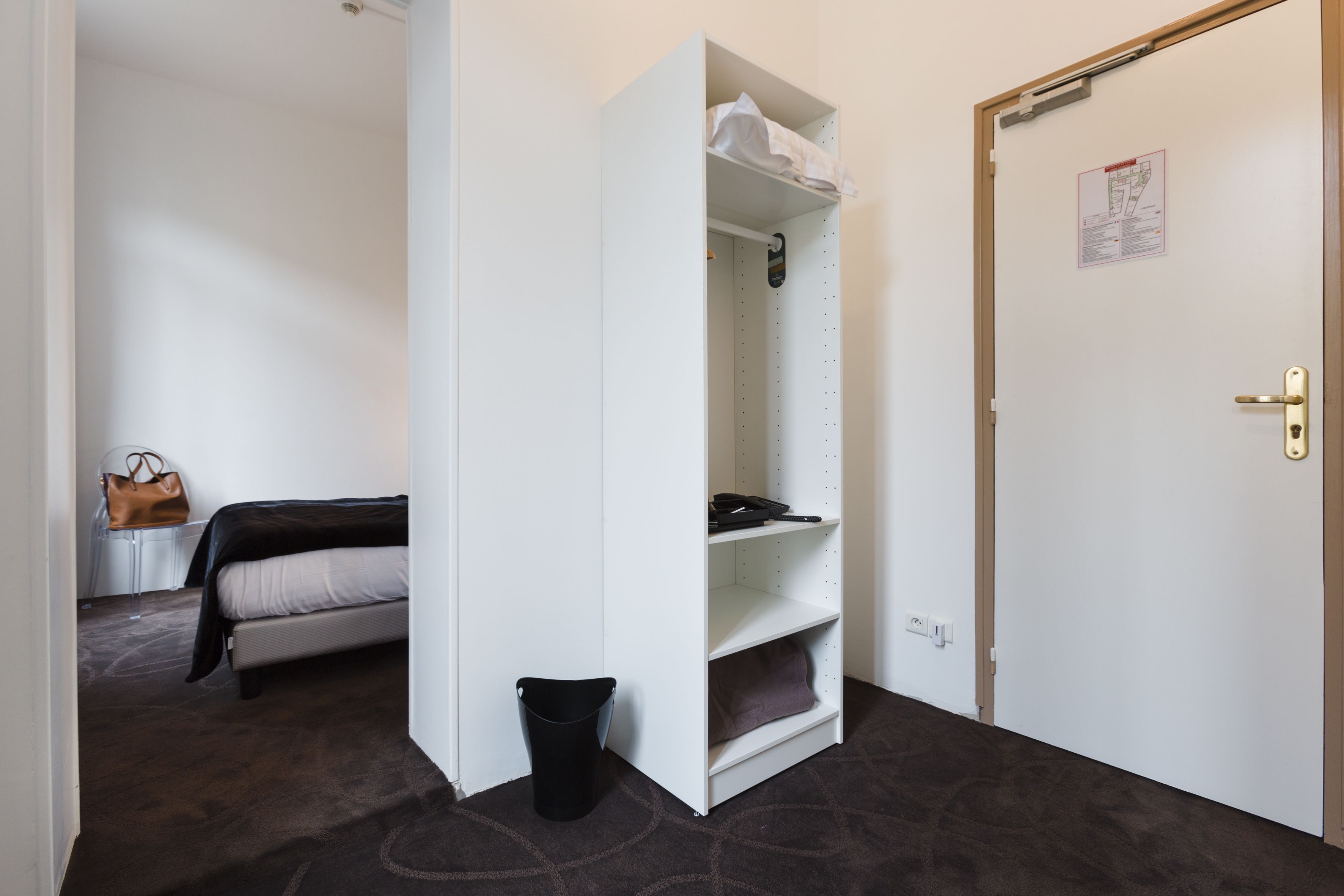 Una habitació d'hotel amb un llit, un armari blanc, un safataire negre i una porta amb un mapa a la paret.