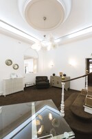 Un salón espacioso con techo alto, una mesa de centro de vidrio, un sofá oscuro, un radiador blanco y una escalera con barandilla de madera.