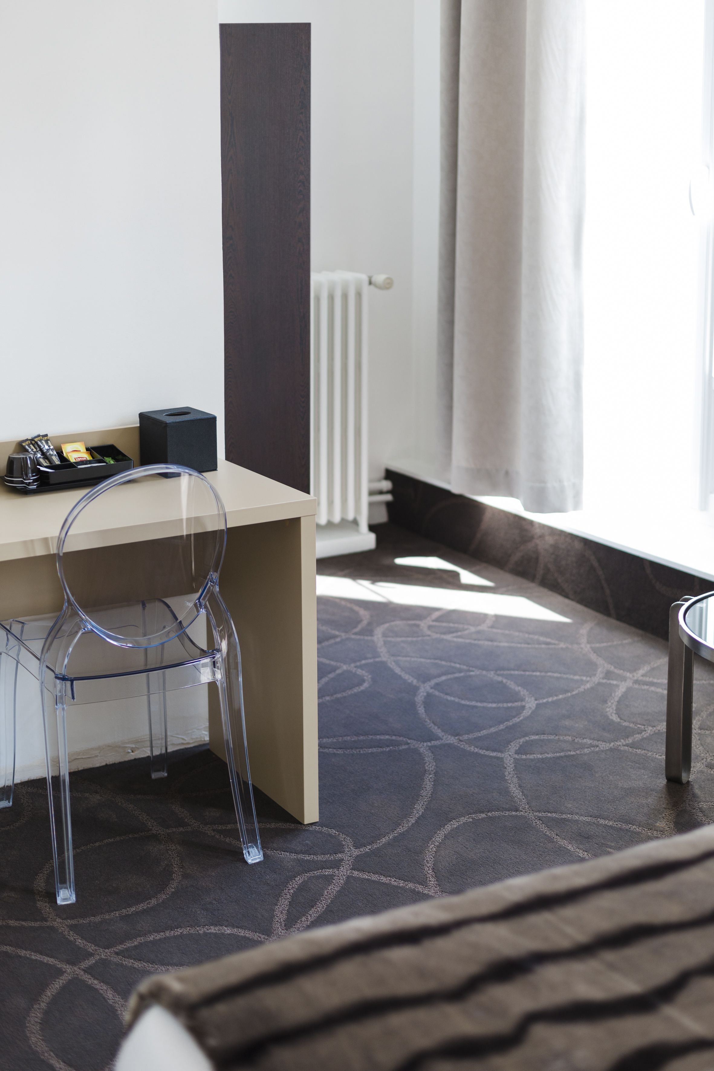 Habitación de hotel con escritorio, silla, radiador y ventana con cortinas.
