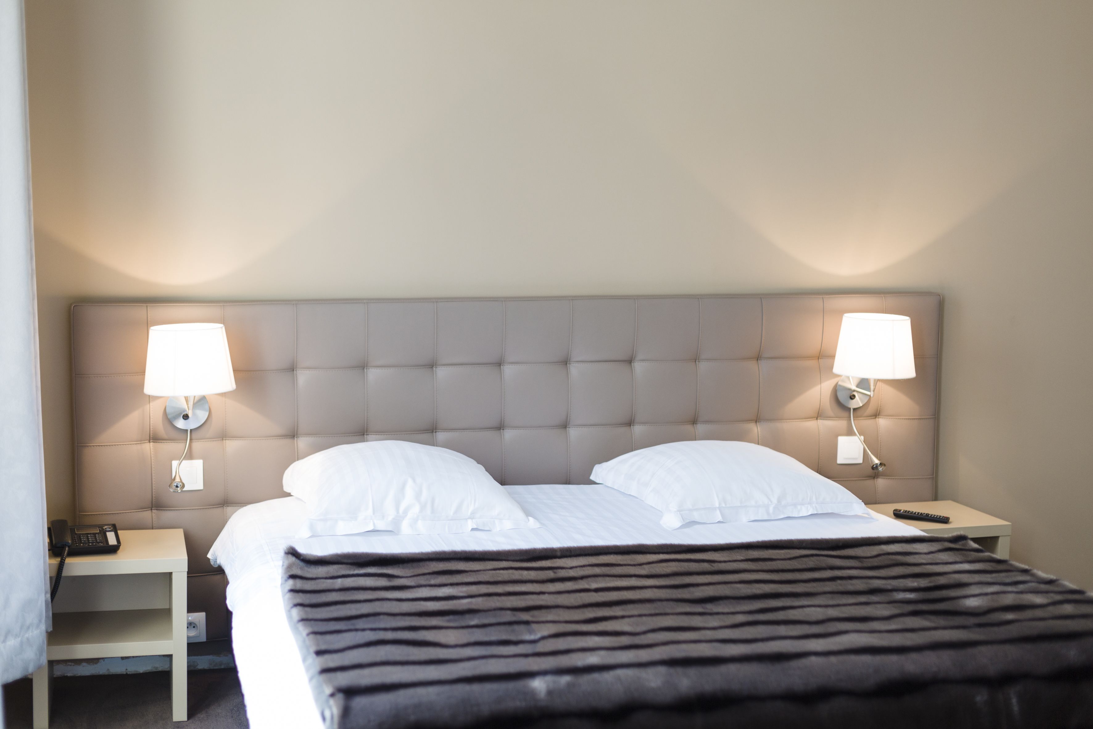 Una habitación de hotel con una cama grande, dos lámparas de noche, una mesita de noche y un control remoto.