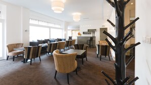 Een moderne hotelentree met een centraal gelegen bar, verschillende zithoeken en een opvallende zwarte kapstok.