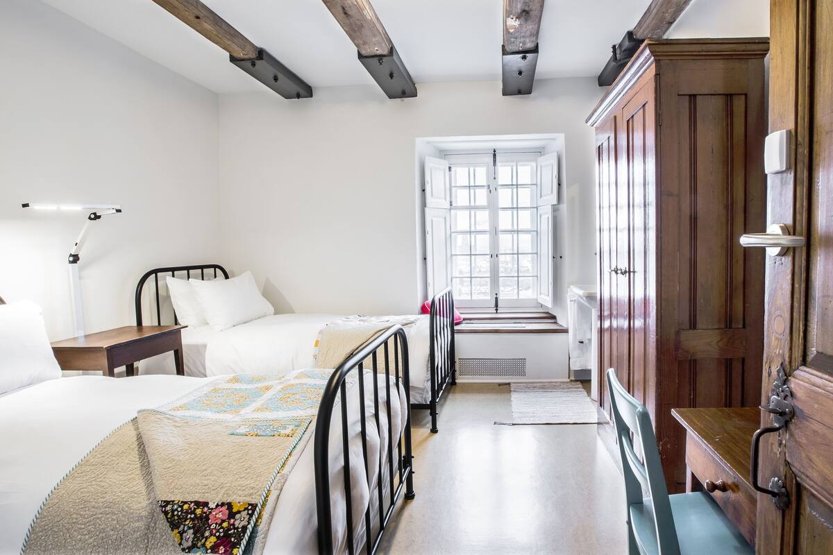 A bedroom with two beds, a desk, a chair, a wardrobe, and a window.