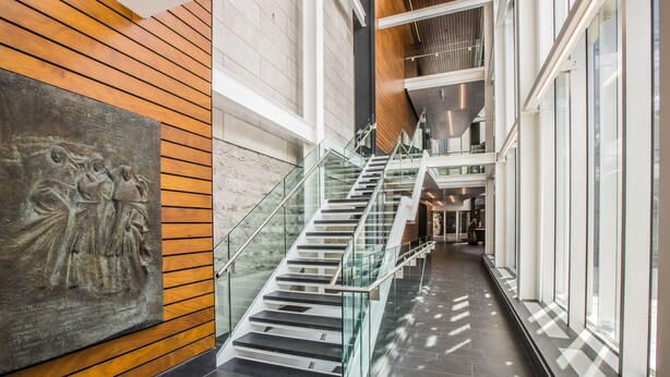 Un interior moderno con una escalera de cristal, paneles de madera y una gran escultura.