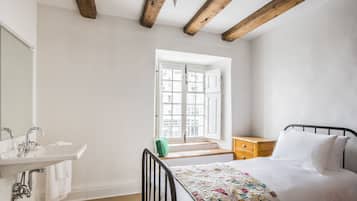 A bedroom with a bed, a window, a wooden ceiling, a bedside table, and a bathroom with a sink and mirror.