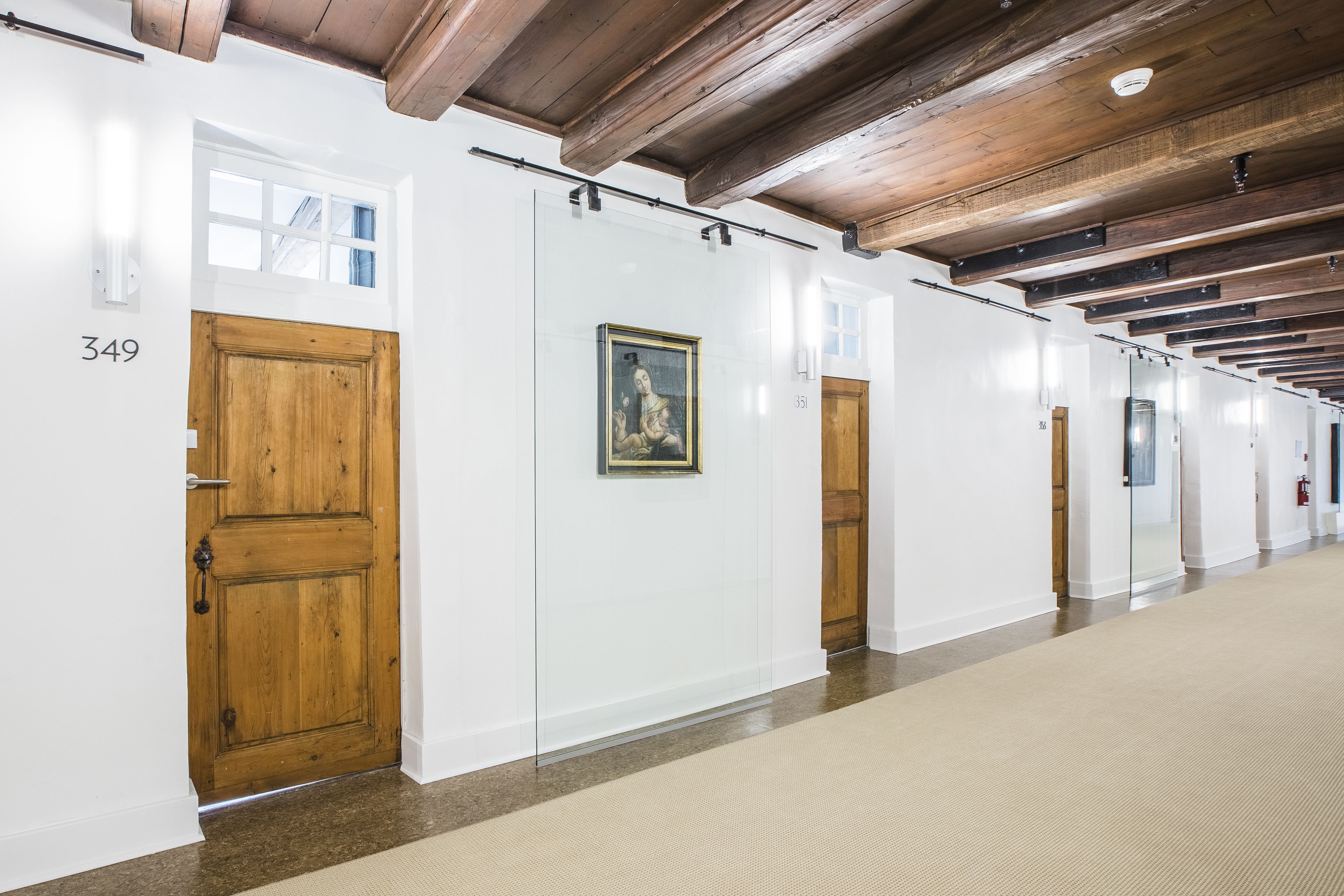A hallway with wooden doors, numbered 349 and 351, and a framed painting on the wall.