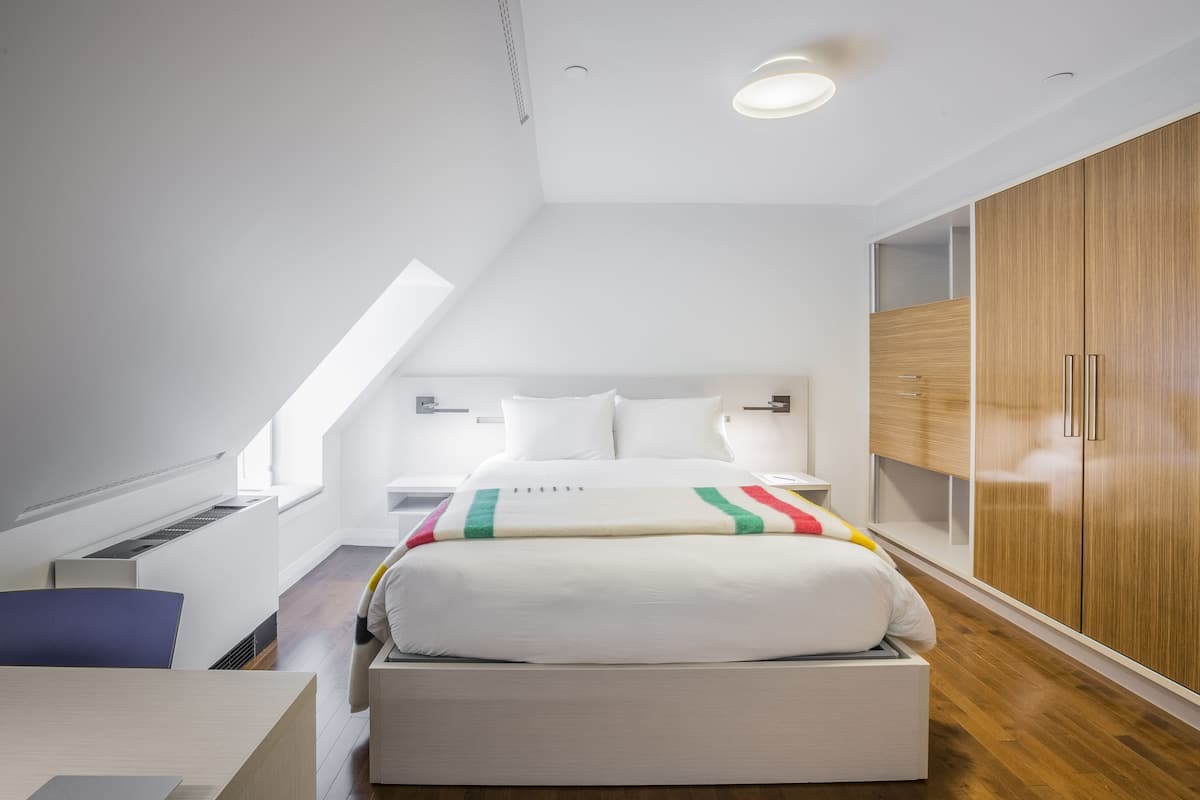A modern bedroom with a loft-style bed, built-in wardrobe, and skylight.