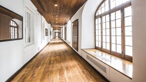 Un largo pasillo con pisos de madera, paredes blancas y amplios ventanales arqueados.