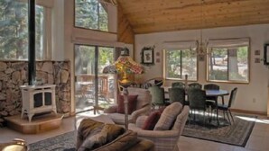 A spacious living room with a stone fireplace, large windows, and a dining area with chairs and a table. - St. Croix (Truckee)