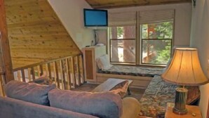 A cozy cabin interior with a wooden staircase, a television mounted on the wall, a cushioned seating area, and a lamp on a side table. - St. Croix (Truckee)