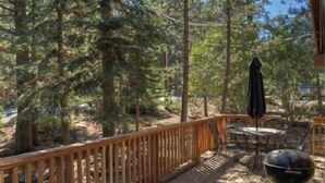 A wooden deck with outdoor furniture and a grill, surrounded by tall trees. - St. Croix (Truckee)