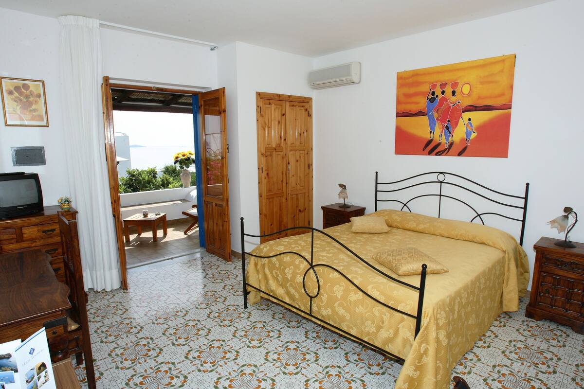 A bedroom with a bed, wooden wardrobe, bedside table, and a painting on the wall.