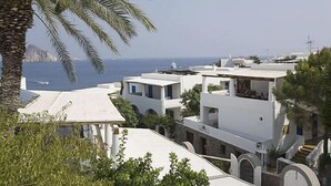A coastal building complex with white exteriors, a palm tree, and a view of the sea. - Hotel Tesoriero (Panarea)