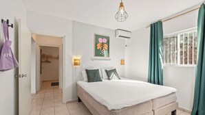 Une chambre à coucher comprenant un lit, un luminaire suspendu, un climatiseur fixé au mur et une fenêtre avec des rideaux.