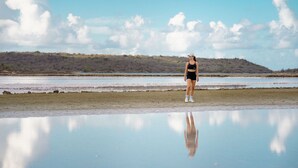 Une personne se tient sur une surface réfléchissante, près d’une étendue d’eau, avec un paysage vallonné en arrière-plan.