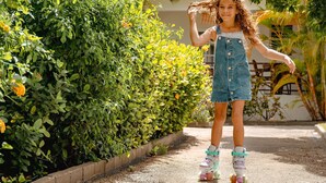 Un enfant fait du roller sur une allée pavée, avec de la verdure et un bâtiment en arrière-plan.