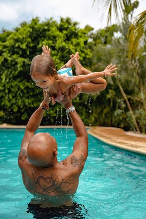 A man lifting a child over a swimming pool with water splashing around. - TUK Tropical Boutique Resort Jan Thiel (Jan Thiel)