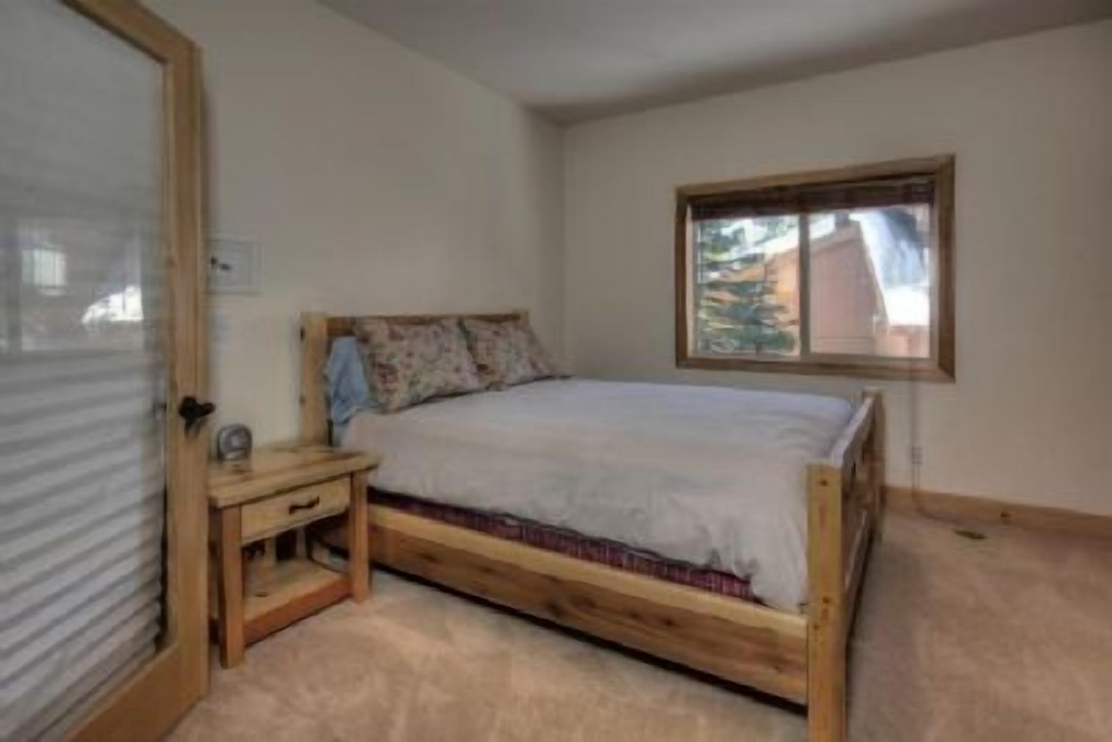 Une chambre à coucher avec un lit en bois, une table de chevet, une fenêtre et une porte.