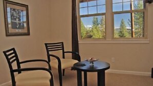 Una habitación con dos sillas y una mesita, un cuadro en la pared y una ventana con vistas a árboles.