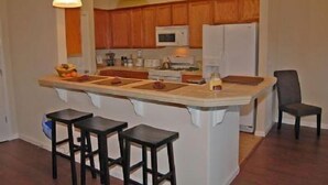 Una cocina con armarios de madera, una isla central con taburetes, un microondas y un refrigerador.