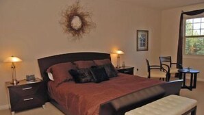 Un dormitorio con una cama grande, dos mesitas de noche, una silla y una pequeña mesa.