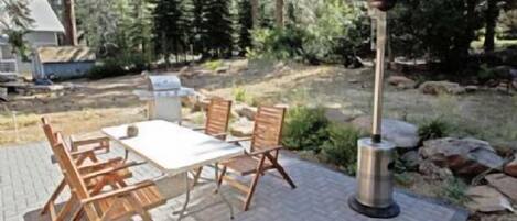 An outdoor patio with a table and chairs, a grill, and a lamp.