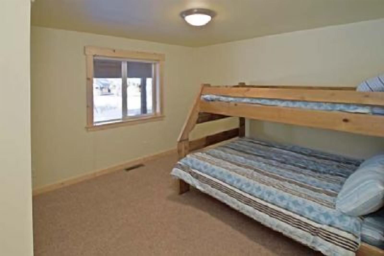 A room with a bunk bed, carpeted floor, a window with blinds, and a ceiling light.