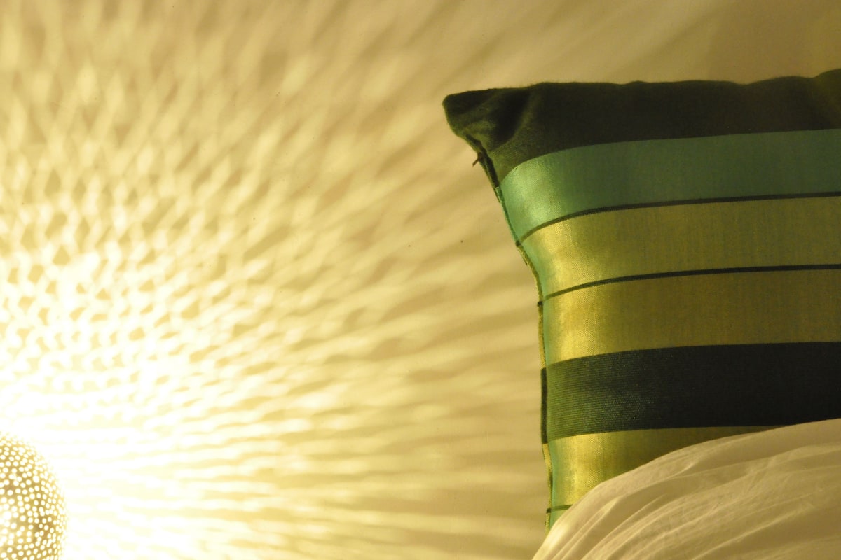 A pillow with green and black stripes on a textured white surface.