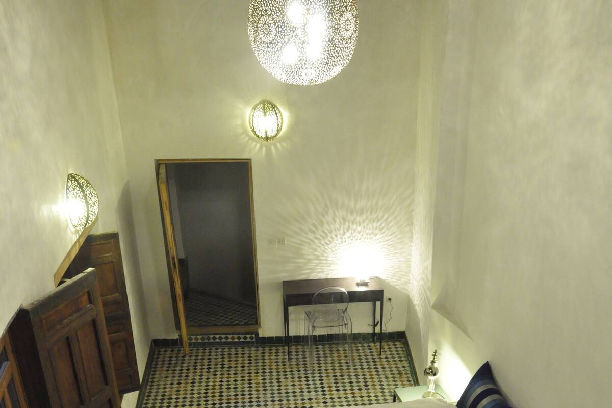 A room with two beds, a wooden wardrobe, a small table with a lamp, and a mirror on the wall.