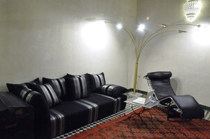 Uma sala de estar moderna com um sofá preto, uma poltrona preta, um abajur e um tapete estampado.