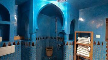 Un baño con paredes azules, un estante de madera con toallas y una zona de ducha.