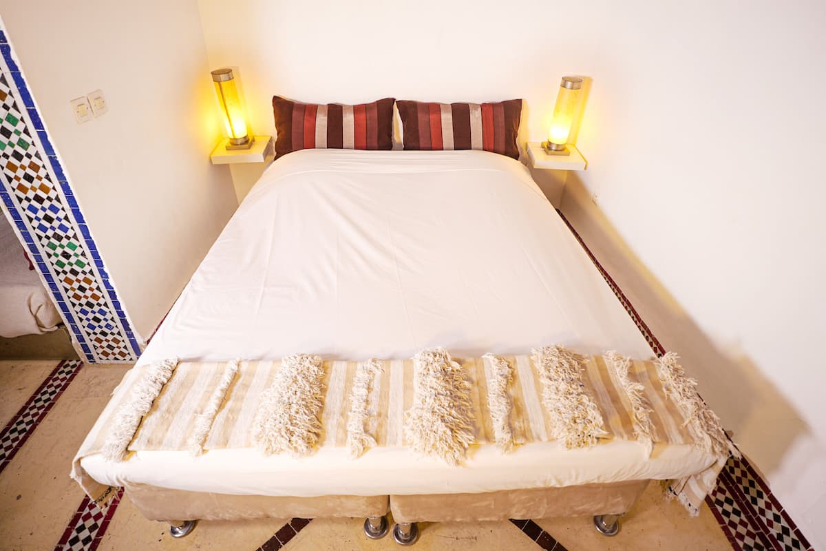A bed with a white mattress and striped pillows, two bedside lamps, and a patterned rug.