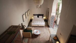 Un dormitorio con cama, mesita de noche, lámpara, un jarrón decorativo y vistas a un espacio exterior a través de un arco.