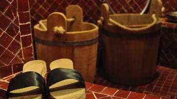 A bathroom with a tiled floor, a wooden bucket, and a pair of black sandals.
