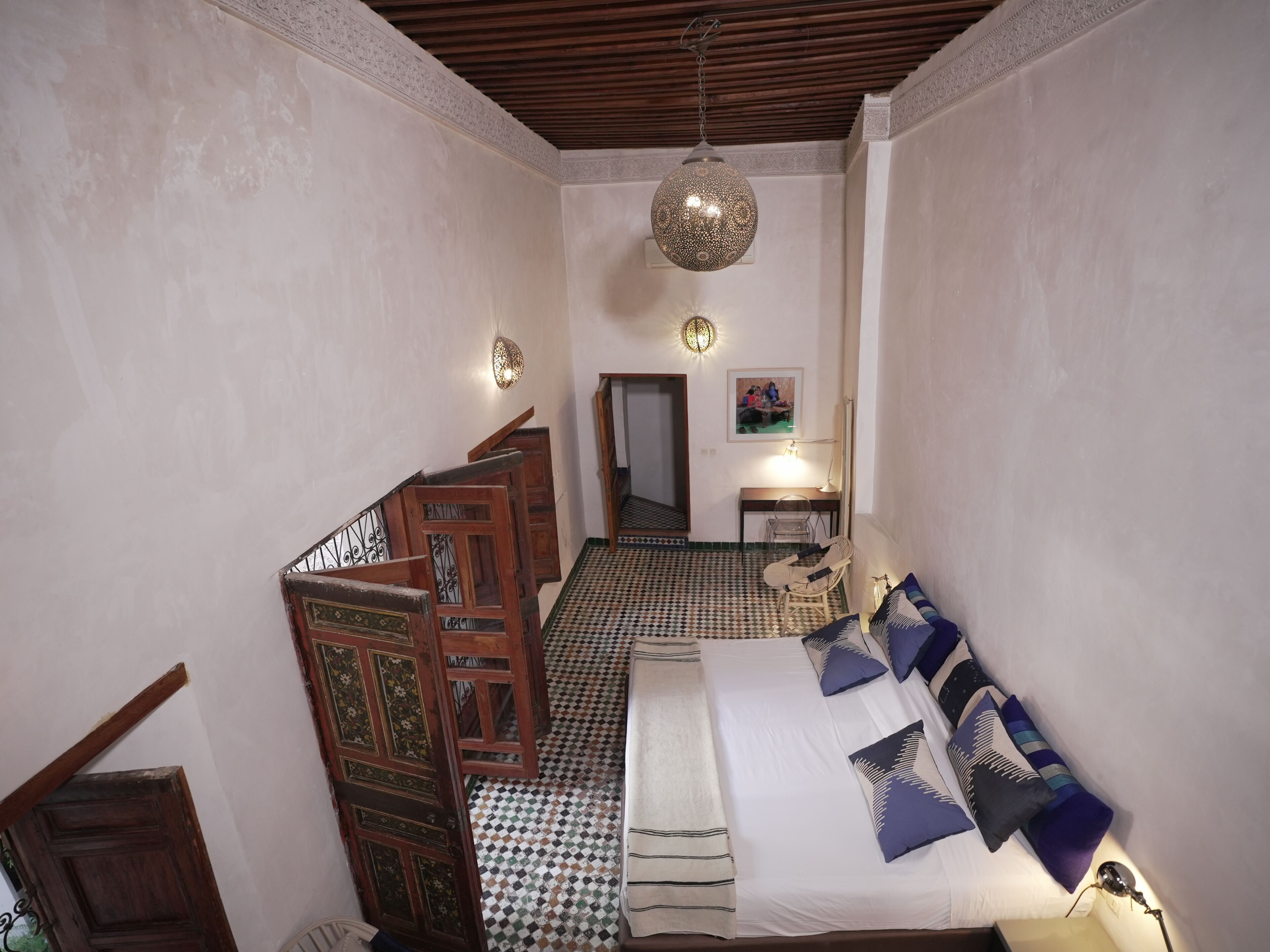 Un dormitorio con piso a cuadros, una cama con almohadas, una escalera de madera y un colgador de luz.
