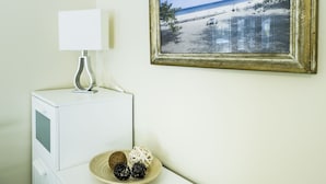 A room with a white desk, a framed beach photograph on the wall, a lamp, and a plate with decorative balls. - Hollywood Cottages (Wasaga Beach)