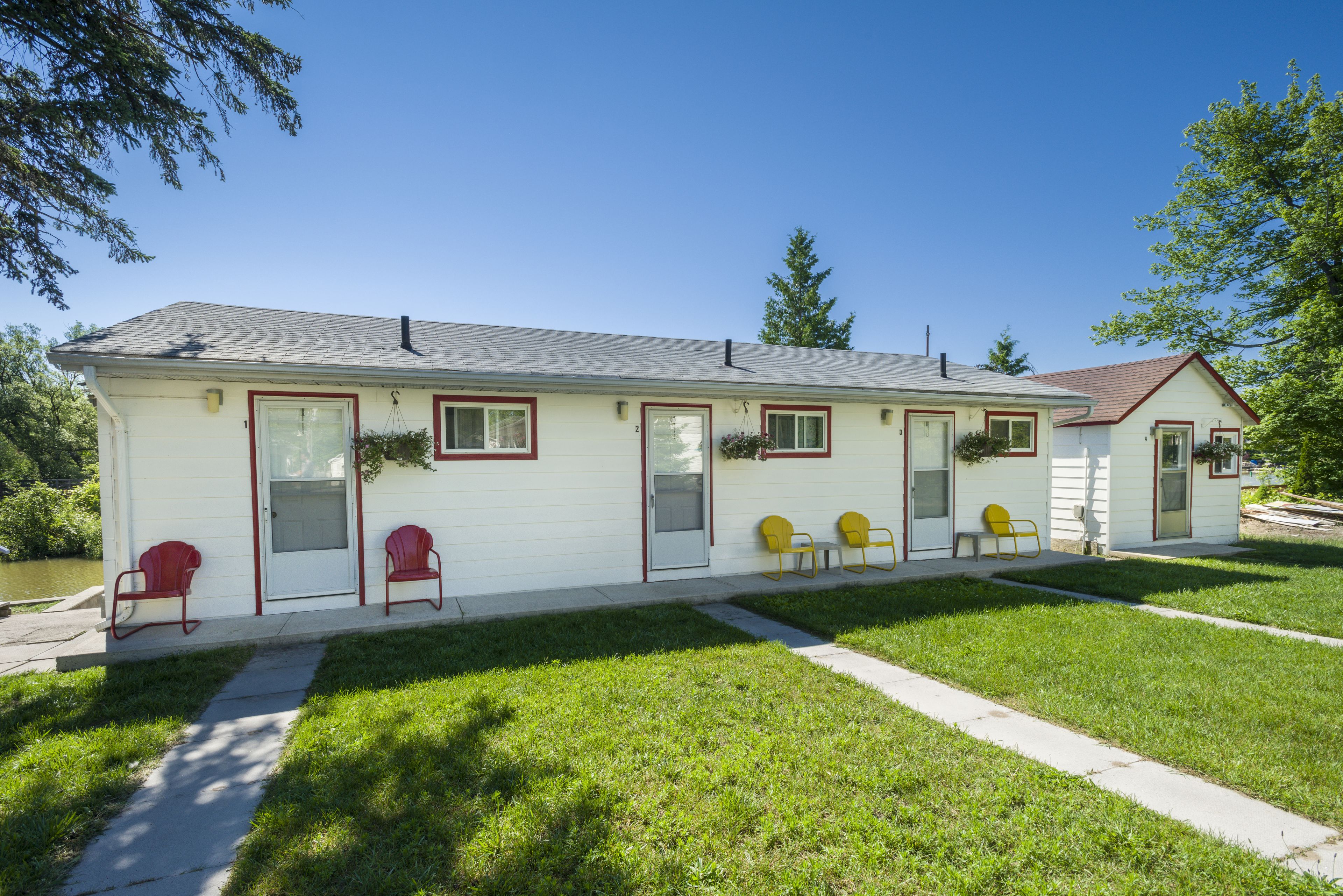 A single-story motel with a red-framed door, a small porch with yellow chairs, and a clear blue sky.