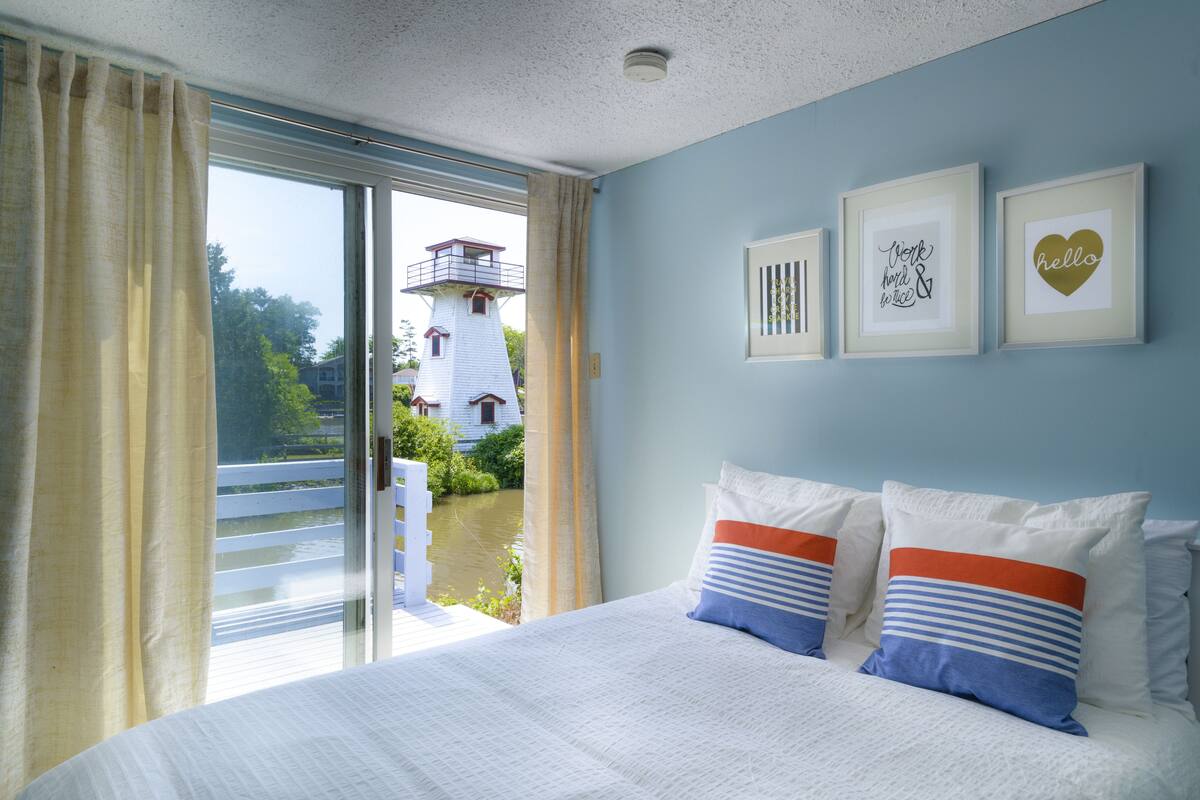 A bedroom with a large bed, a view of a lighthouse, and framed artwork on the wall.