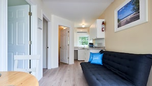A compact living space with a kitchenette, a sofa with a blue pillow, and a framed picture on the wall. - Hollywood Cottages (Wasaga Beach)