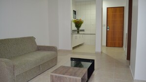 A living room with a sofa, a coffee table, and a kitchen area visible through an open doorway.