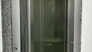 A metallic elevator with a glass door, a control panel, and a small circular object on the wall.
