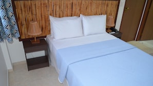 A neatly made bed with white linens and a blue striped blanket, a wooden headboard, a bedside lamp, and a nightstand with a phone and lamp.