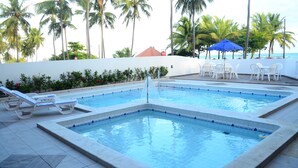 A swimming pool with two sections, surrounded by palm trees and a beach view.