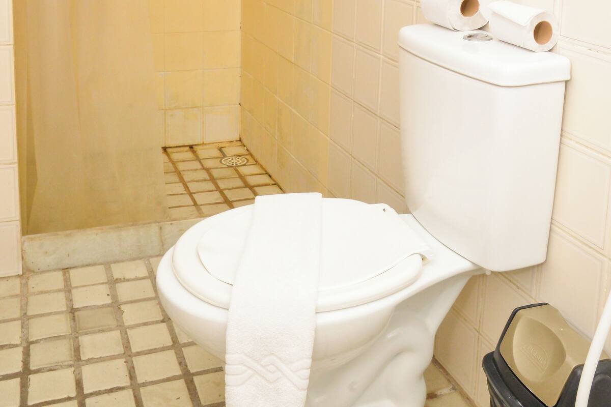 Un baño con inodoro, cortina de ducha y cubo de basura.