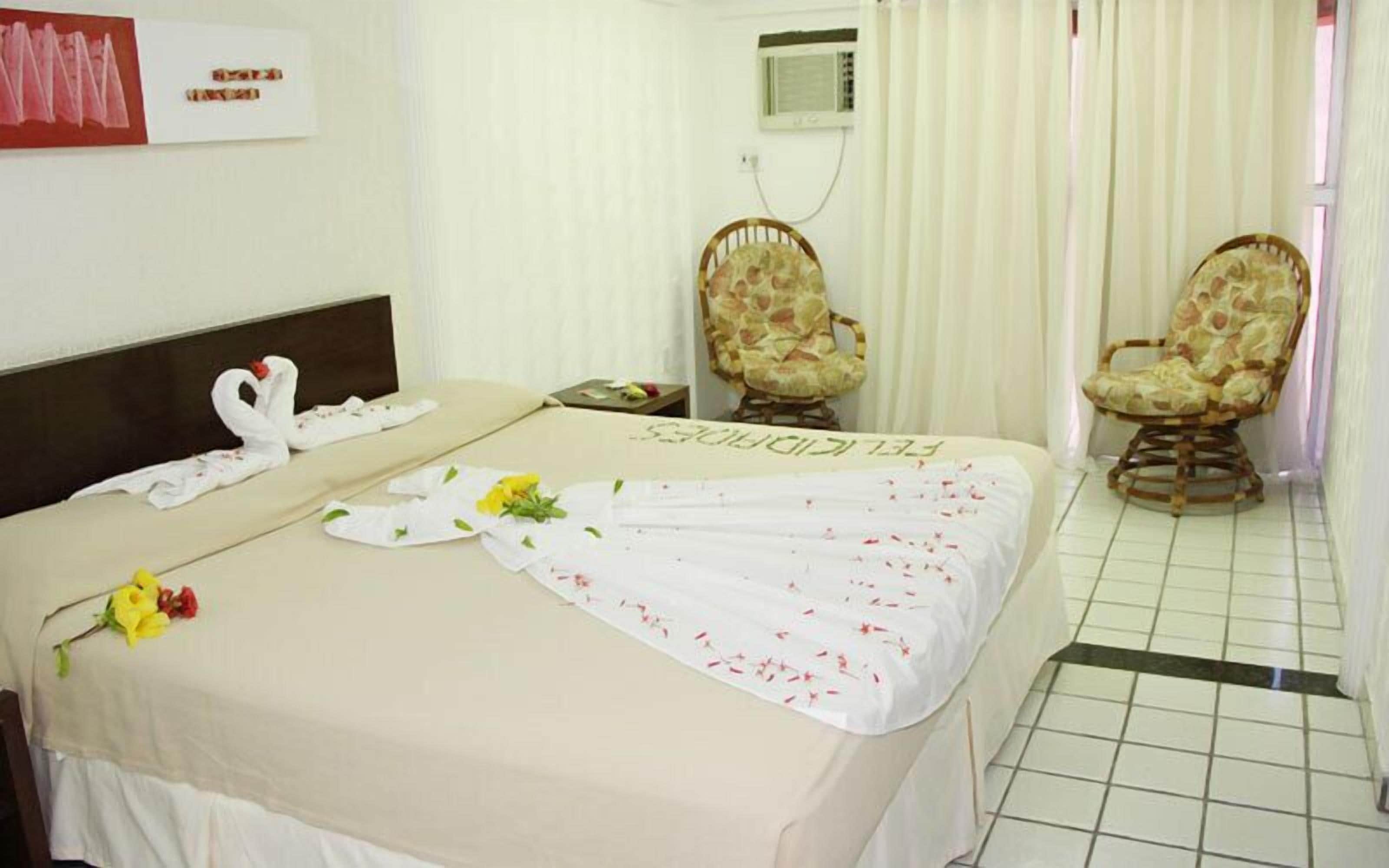A hotel room with a bed, two chairs, a wall-mounted air conditioner, and a tiled floor.