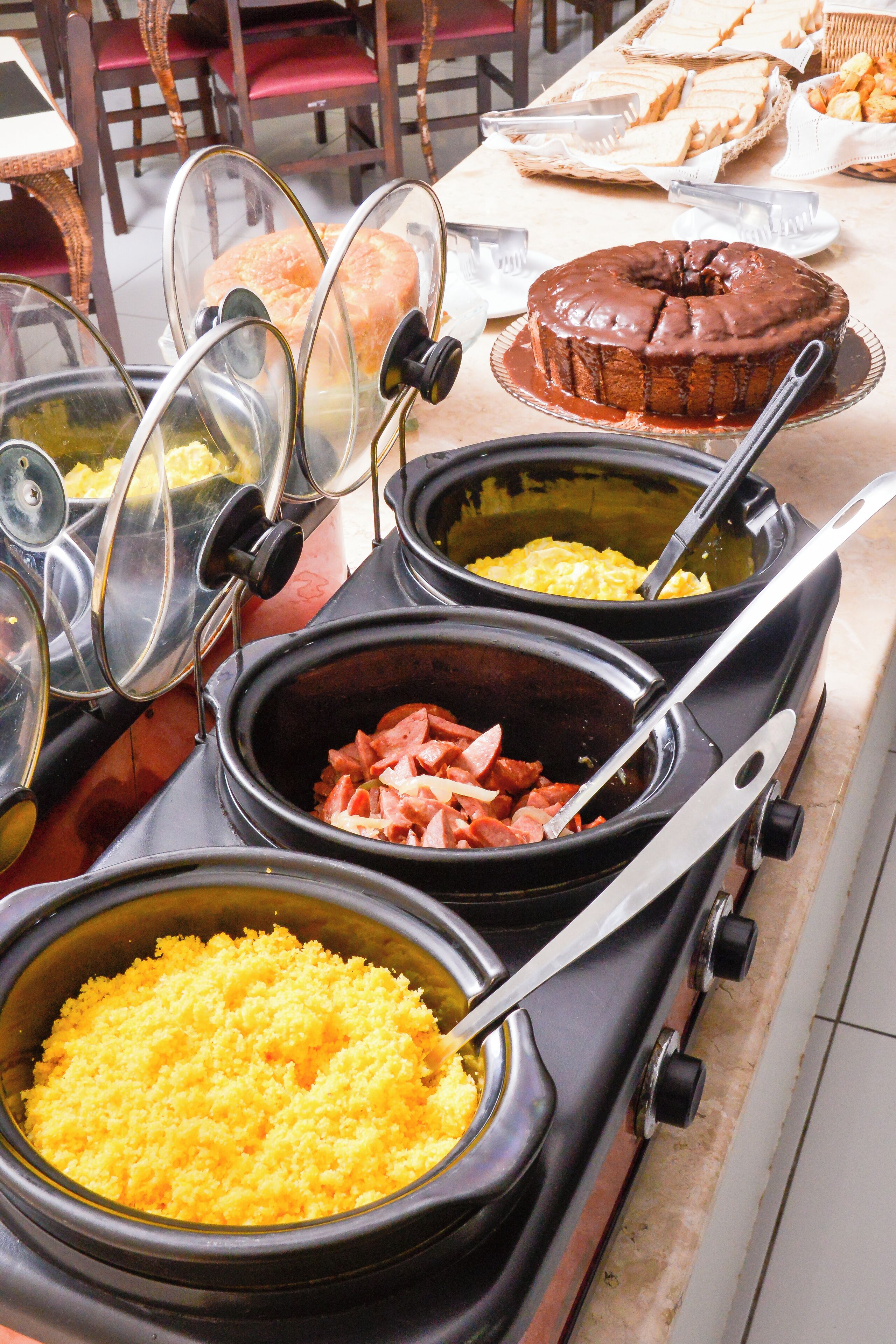 A buffet with various food items including scrambled eggs, ham, and a chocolate cake.