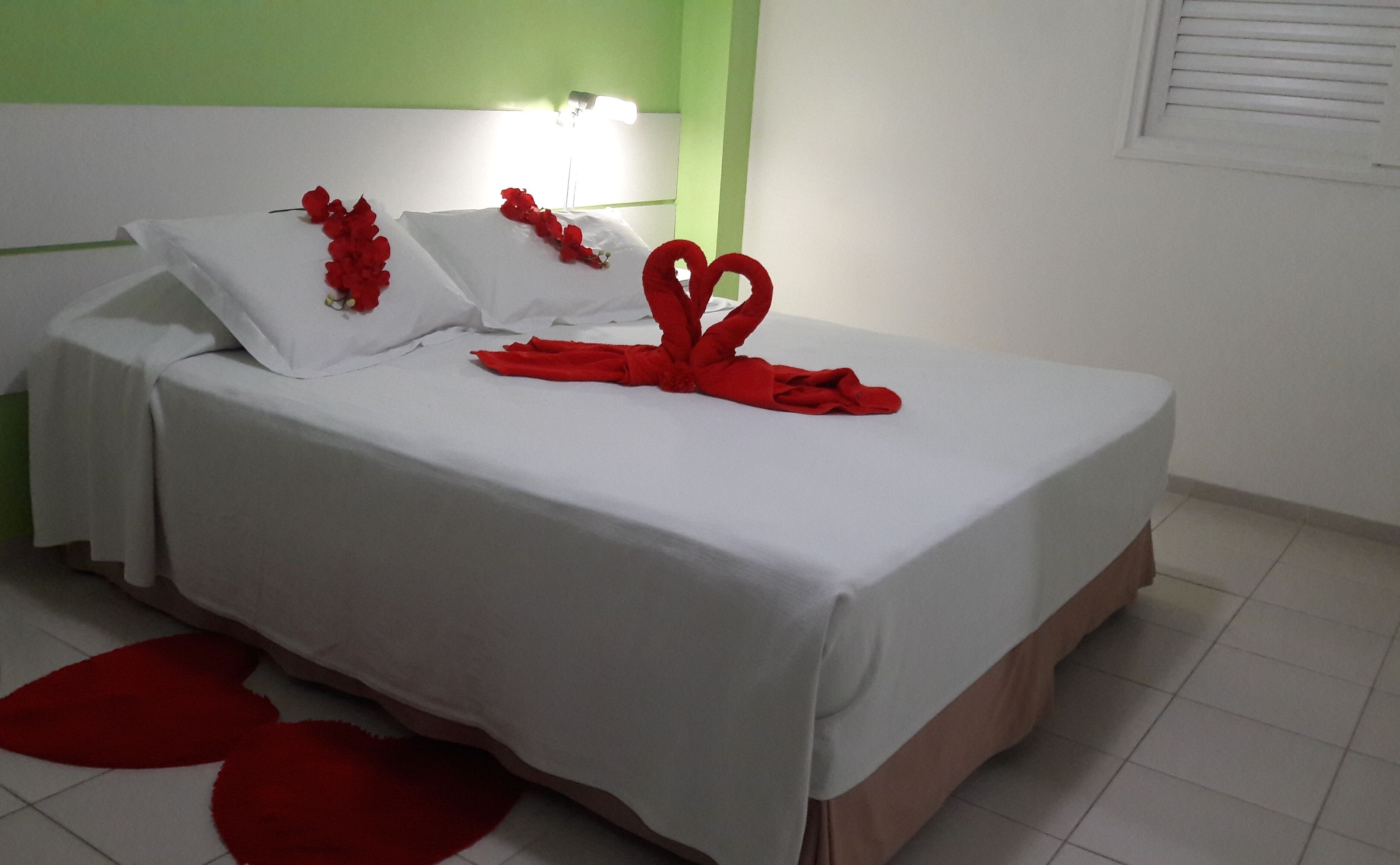 A hotel room with a bed, white bedding, and red decorations.
